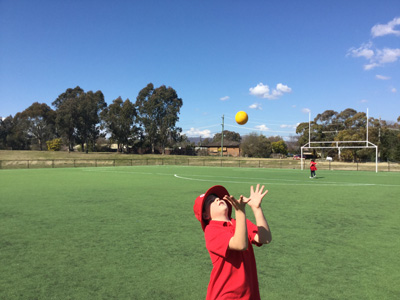 A student is catching a ball on the oval.